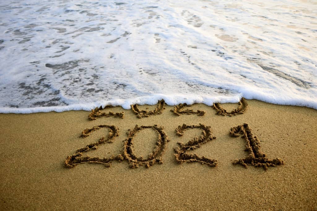 Ocean wave washing over 2020 as 2021 appears in the sand