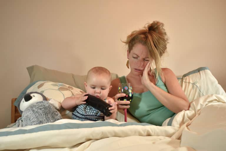 Frazzled mother in bed with her child and with a glass of wine appearing exhausted