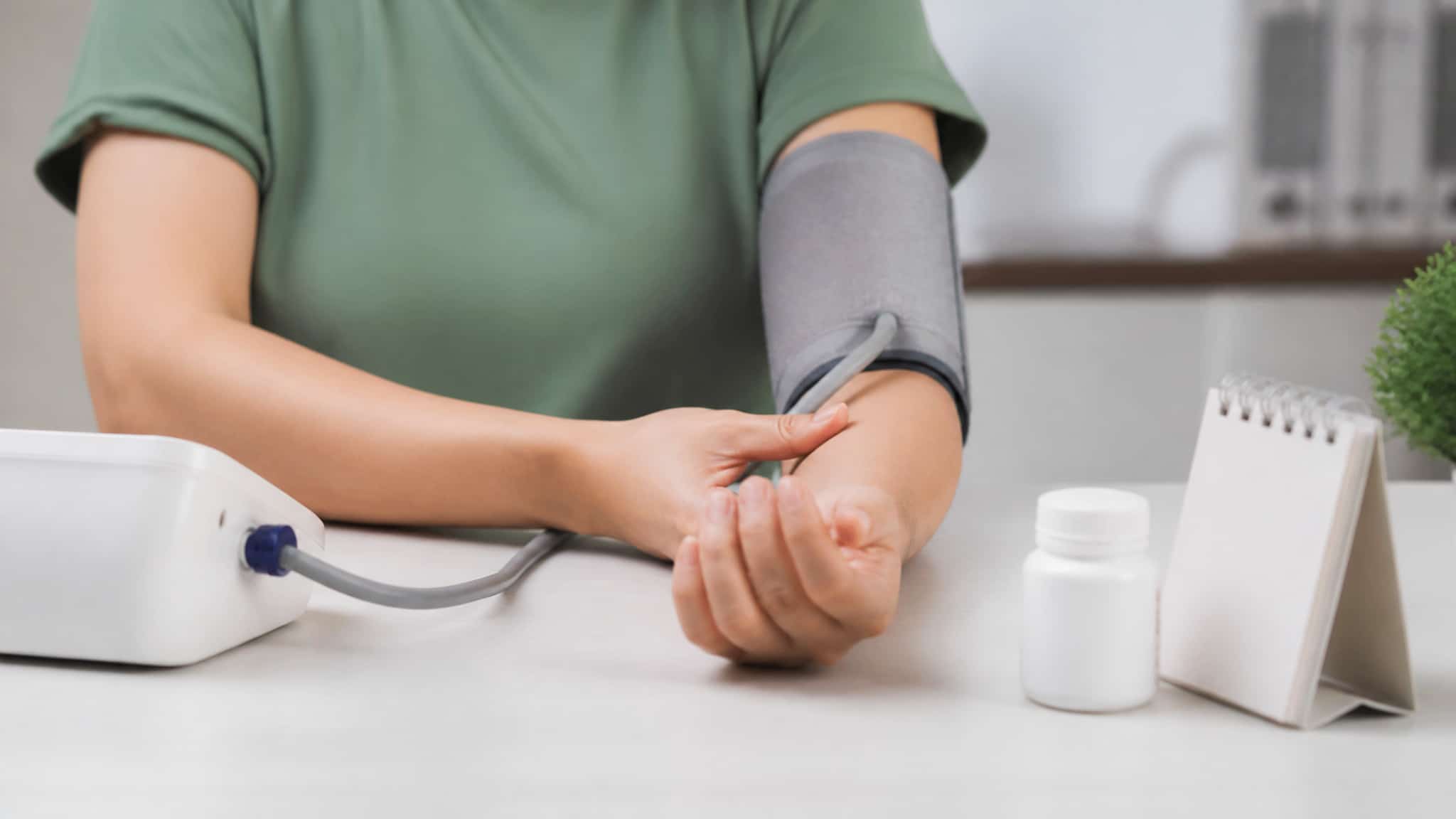 Person wearing a blood pressure cuff and holding their wrist beside a medicine bottle and desk calendar.