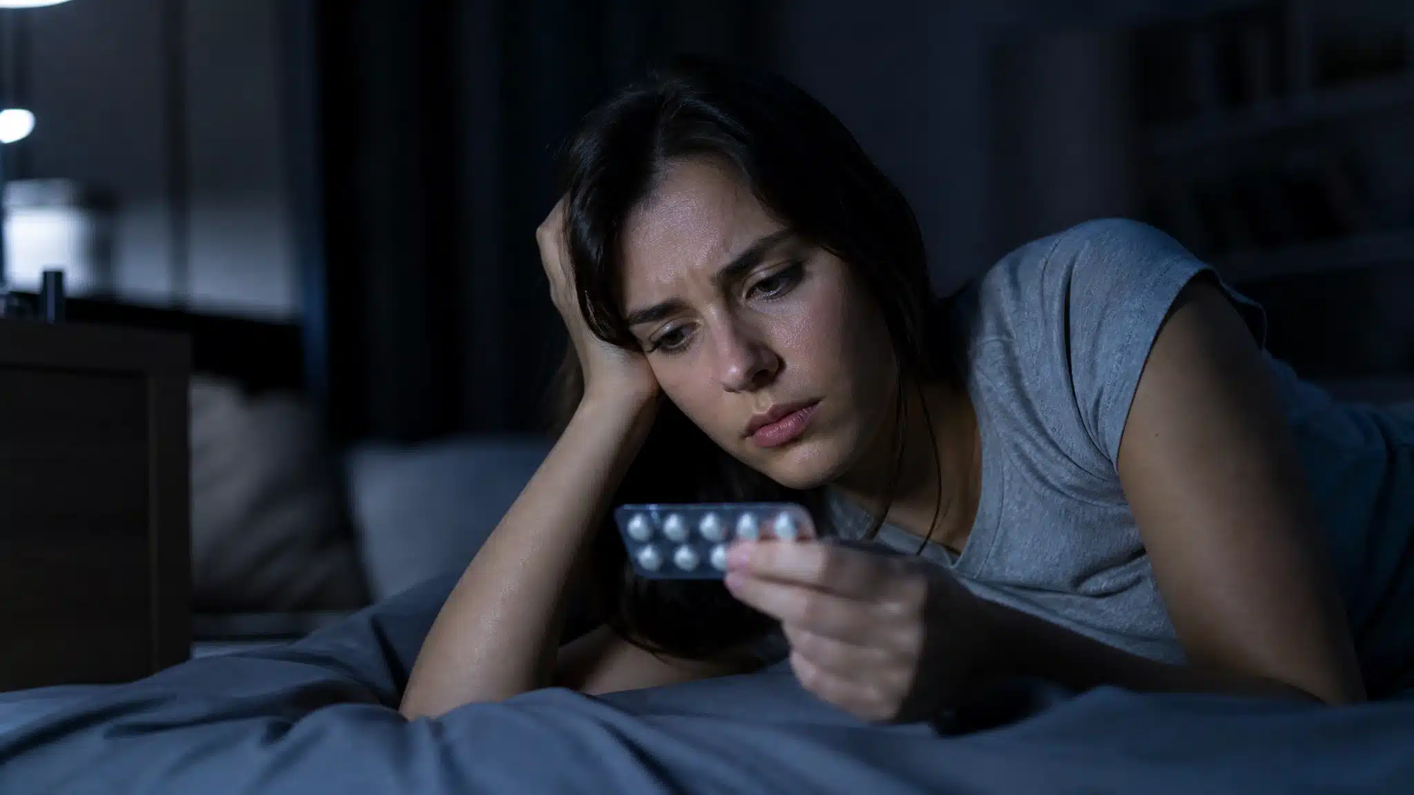 Woman lying on a bed looking at a blister pack of pills